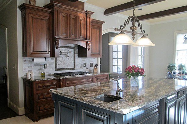 Granite topped island with an undermount sink below pendant lights, beside dark cherry cabinetry