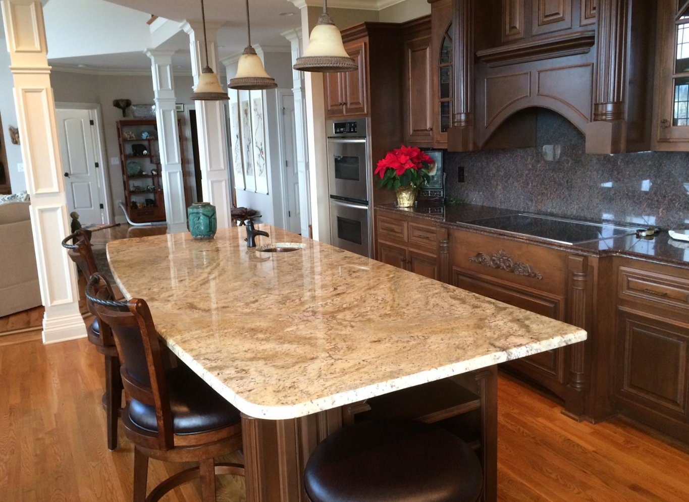 Cream and gold granite island with a rounded edge in a kitchen with dark stained cabinets and double ovens